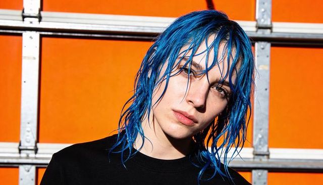Posing woman with wet blue hair wearing black shirt against orange metal garage door urban