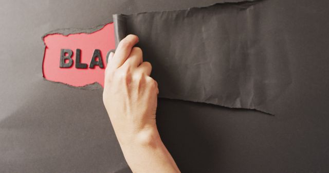 Hand tearing black paper to reveal a red background with text. Perfect for creative concepts, advertisement layouts, and motivational posters. Could be used in designs emphasizing discovery, unveiling hidden messages, or emphasizing the contrast between different ideas.