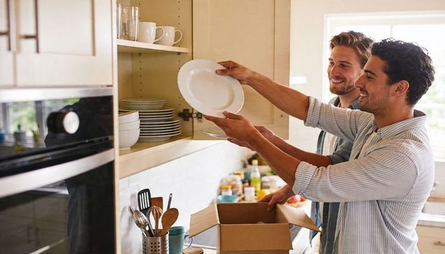 Unpacking together: young men organizing dishware in sunlit modern kitchen during move