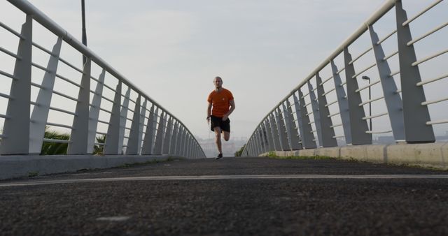 Man jogging on an urban bridge during a morning workout, showcasing a healthy and active lifestyle. Ideal for use in fitness advertisements, health and wellness promotions, and urban lifestyle campaigns.