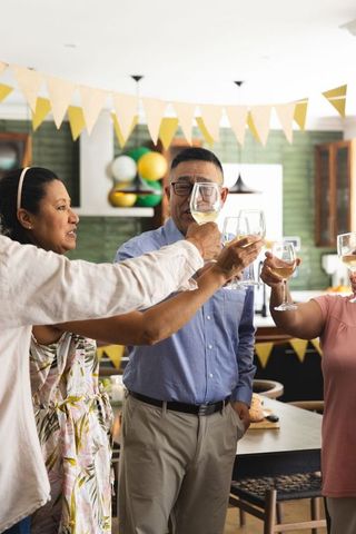 Mature friends toasting wine during cozy kitchen celebration with bunting and balloons