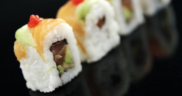 Sushi rolls with vibrant toppings are presented in a row on a sleek, dark surface, with copy space. Their meticulous preparation suggests a culinary art form, inviting a taste of traditional Japanese cuisine.