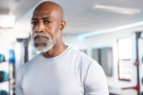 Senior african american man in gym wearing light gray athletic shirt showing calm strength