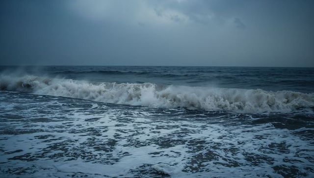 Rolling crashing ocean waves under overcast sky with foamy surf and sea spray