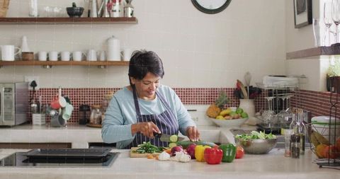 Senior indian home cook chopping vegetables on kitchen island preparing healthy meal