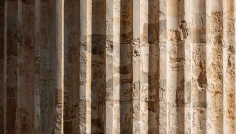 Worn fluted stone masonry wall with shadow bands, horizontal seam and weathered patina