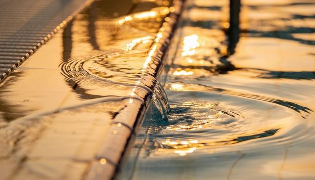 Golden hour pool overflow creating flowing water sheet and concentric ripples close-up