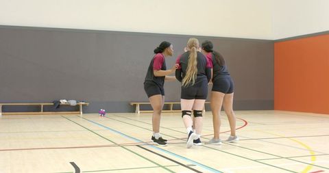 High school volleyball team huddling on indoor court showing support and knee brace