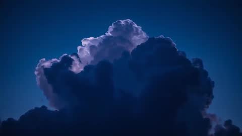 Towering thundercloud rising at twilight with dramatic backlit silver lining and deep blue sky