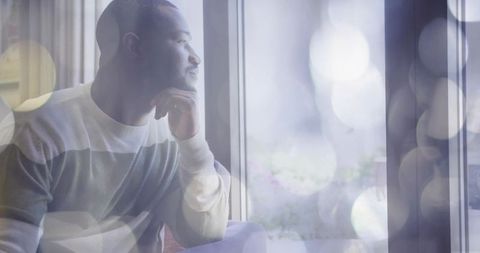 Contemplative man gazing out window in cozy living room with soft bokeh light