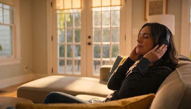 Sunlit living room woman listening to music with over-ear headphones relaxing on sofa
