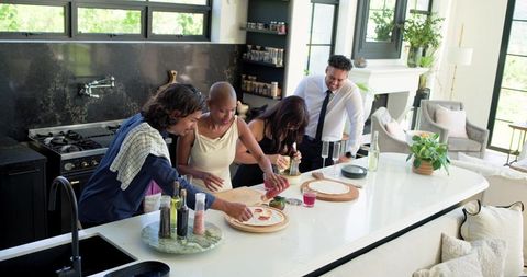 Friends preparing flatbreads on marble kitchen island during open-plan home gathering