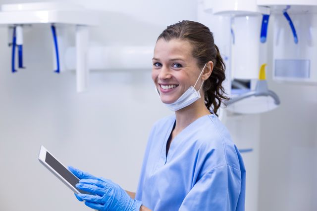 Dental assistant smiling while using a digital tablet in a modern dental clinic. Ideal for use in healthcare, dental care, and technology-related content. Can be used for promoting dental services, showcasing modern dental practices, or illustrating professional healthcare environments.