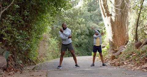 African american father and son stretching on sunlit woodland trail for family fitness