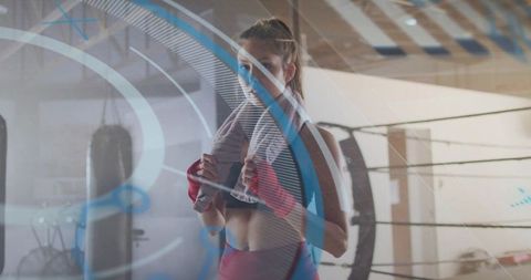 Female boxer training with towel and red hand wraps by heavy bag with neon hud