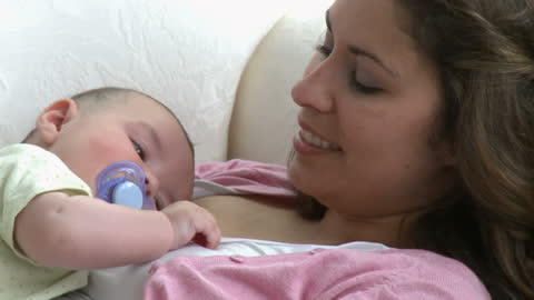 Smiling Mother Relaxing on Sofa with Newborn Baby
