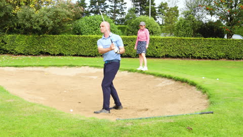 Golfer Swinging from Sand Trap with Spectator on Green Golf Course