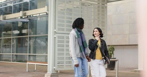 Colleagues walking and talking on modern plaza with glass facade holding notebooks