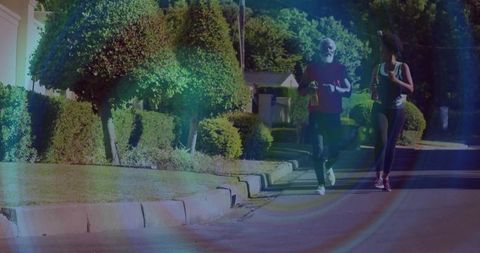 Older man and young woman jogging with water bottles on suburban street, sunshine lens flare