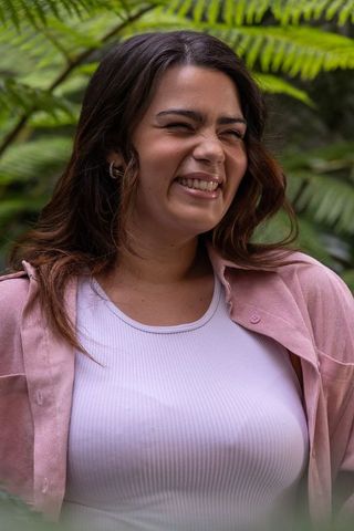 Young woman smiling among ferns wearing white tank and pink shirt, natural portrait