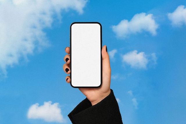 Hand Holding Smartphone Against Blue Sky with Clouds