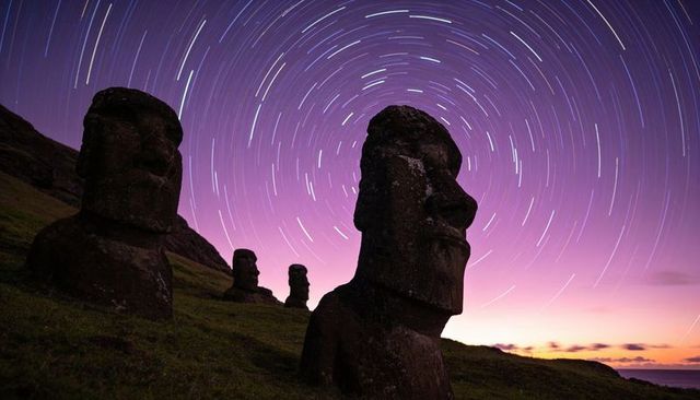 Moai statues under circular star trails at twilight on easter island coastal ridge ancient basalt