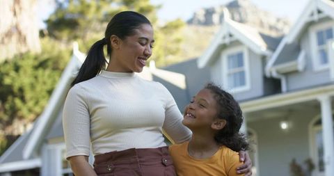 Smiling mother and daughter hugging on front porch of suburban home
