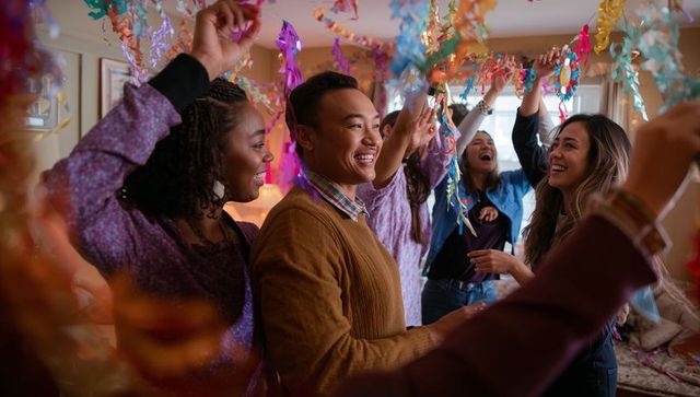 Multicultural friends celebrating at home smiling asian man adjusting colorful streamers