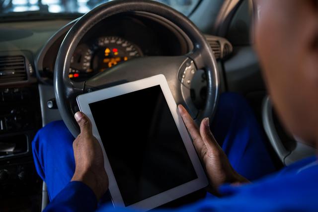 Mechanic using digital tablet for diagnostics in car at repair garage. Useful for illustrating modern automotive repair, technology in vehicle maintenance, and professional mechanic services.