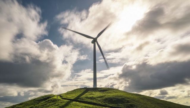 Spinning wind turbine on green hilltop casting long diagonal shadow under dramatic sky
