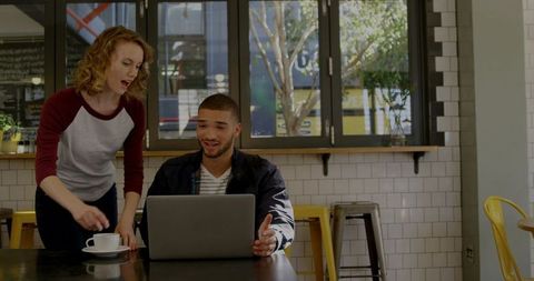 Casual coworking duo collaborating over laptop in bright urban cafe with coffee and teamwork