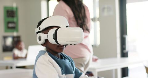 African American boy experiencing virtual reality in classroom while teacher observing