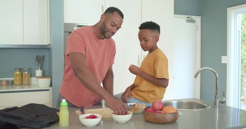 African american father preparing lunch with teen son at modern kitchen island