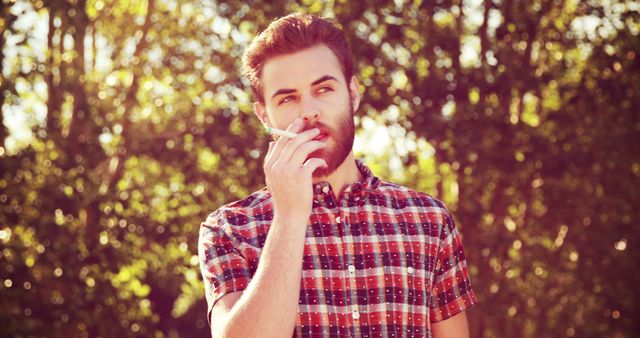 Contemplative Young Man Smoking Outdoors in Natural Setting - Download Free Stock Images Pikwizard.com