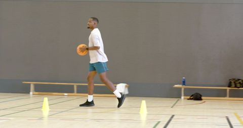 Male athlete dribbling basketball through cones in indoor gym training and agility drill