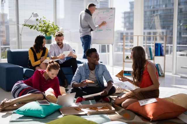 Group of young professionals sitting and discussing work in a modern office environment while enjoying pizza. Ideal for use in articles related to teamwork, modern office culture, casual workspaces, business meetings, and creative brainstorming sessions.