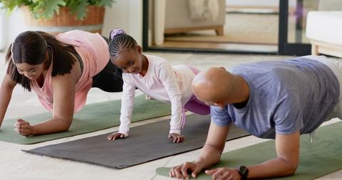 Family doing forearm plank workout together in living room with african american child
