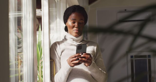 Young African American Woman Using Smartphone Near Window - Download Free Stock Images Pikwizard.com