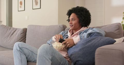 Middle-aged man relaxing on sofa holding popcorn and remote watching tv at home