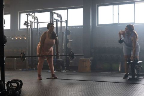 African american women lifting barbell and rowing dumbbell in industrial gym workout