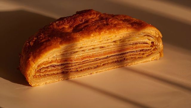 Layered puff pastry slice glowing in warm sunlight on white ceramic plate