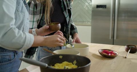 Friends preparing breakfast at kitchen island stirring scrambled eggs modern home cooking