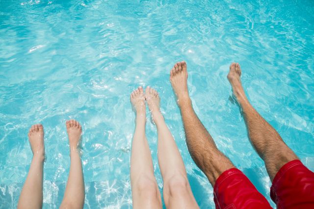 Low section of family sitting on poolside and shaking their legs in pool water