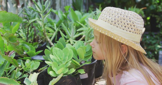 Caucasian girl wearing hat looking at plants with green leaves in garden. Childhood, nature, gardening and hobbies.