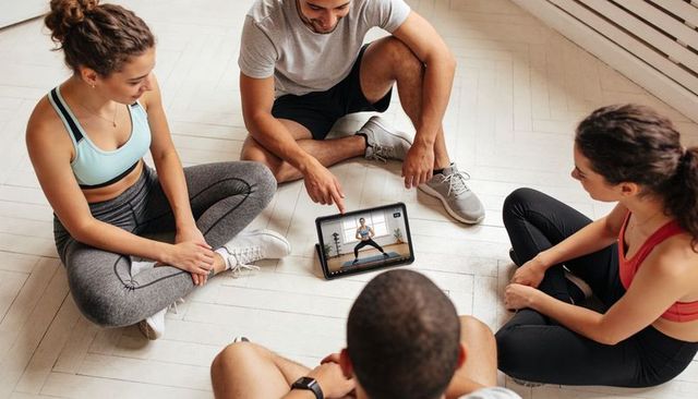 Four adults watching virtual workout on tablet preparing for home fitness training