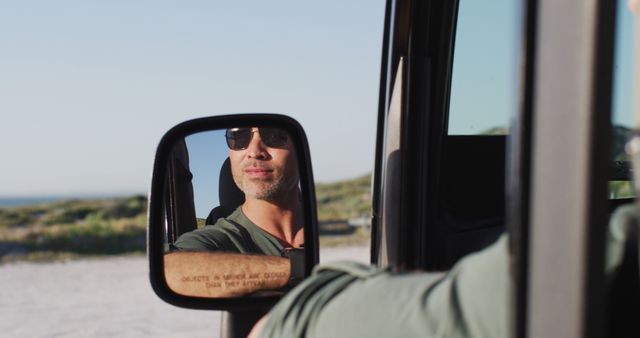Happy caucasian man in sunglasses sitting in car reflected in side mirror on sunny day at the beach. summer road trip and holiday in nature.
