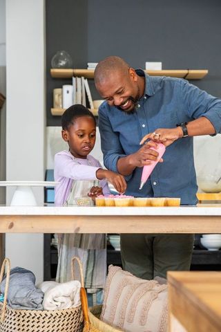 African american father and daughter decorating cupcakes together on kitchen island