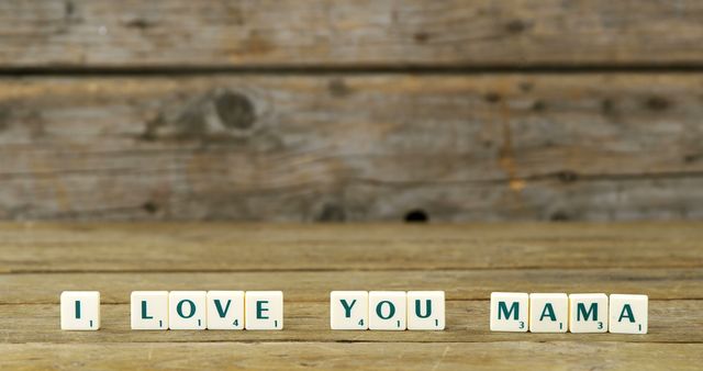Scrabble tiles spell out I LOVE YOU MAMA against a rustic wooden background, with copy space. It's a heartfelt message that could be used for Mother's Day or to express affection and gratitude to mothers.