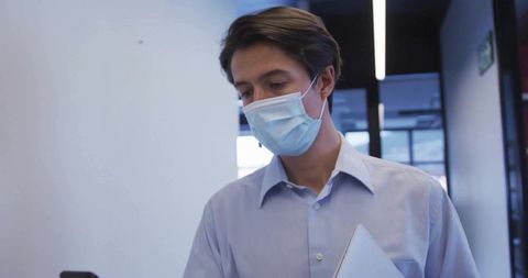 Professional man with mask checking smartphone in office corridor