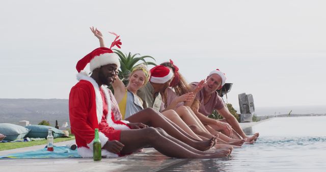 Six diverse happy friends celebrating christmas in costumes, outdoors with feet in swimming pool. Christmas, celebration, tradition, friendship, inclusivity and lifestyle concept.
